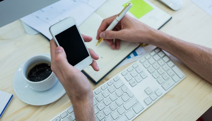 maos-de-designer-grafico-homem-escrevendo-em-um-diario-e-prende-o-telefone-movel.jpg